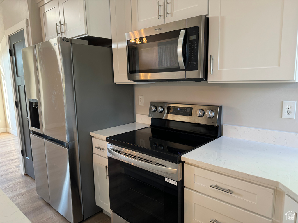 Kitchen with white cabinets, stainless steel appliances, light hardwood / wood-style flooring, and light stone counters