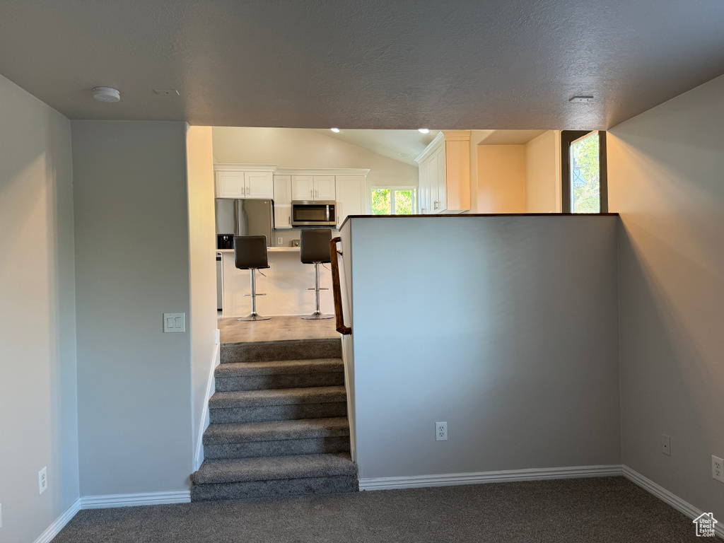 Stairs with dark colored carpet and lofted ceiling