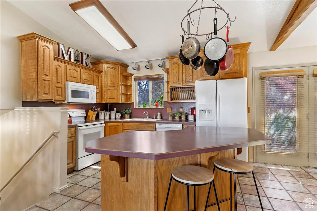 Kitchen featuring white appliances, light tile patterned floors, a kitchen island, a kitchen breakfast bar, and sink