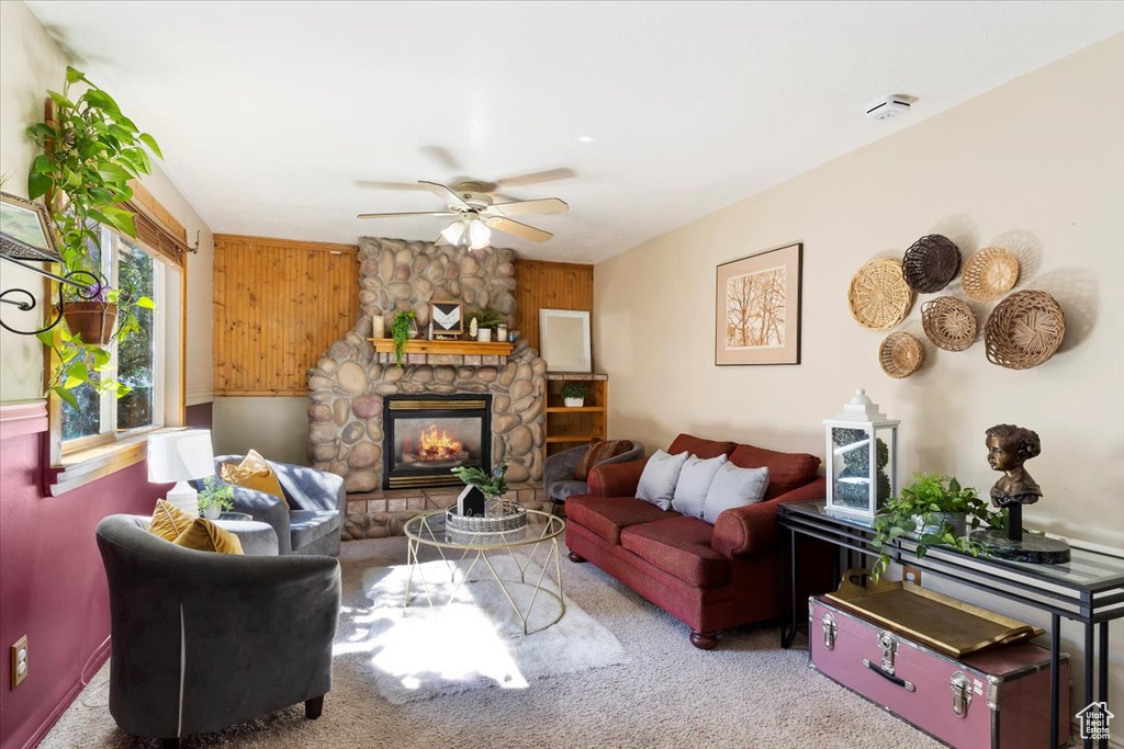 Carpeted living room with wood walls, a fireplace, and ceiling fan