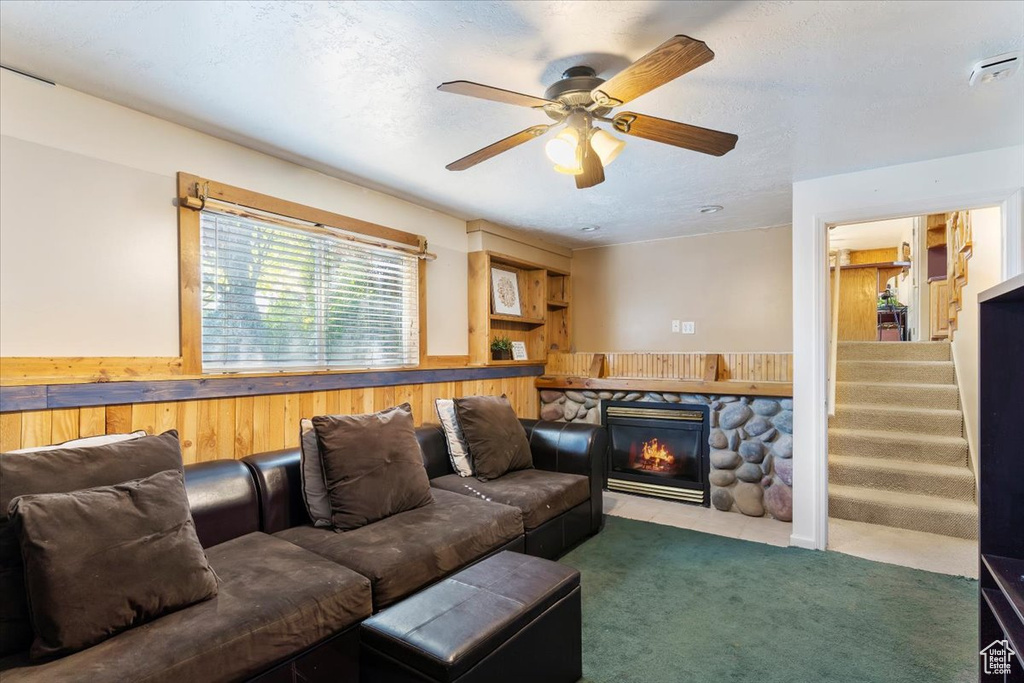 Carpeted living room featuring a stone fireplace and ceiling fan