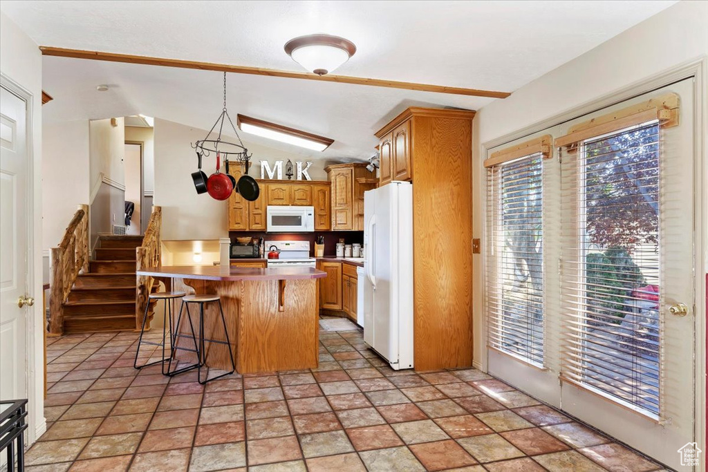 Kitchen with a kitchen island, a breakfast bar area, white appliances, and light tile patterned floors