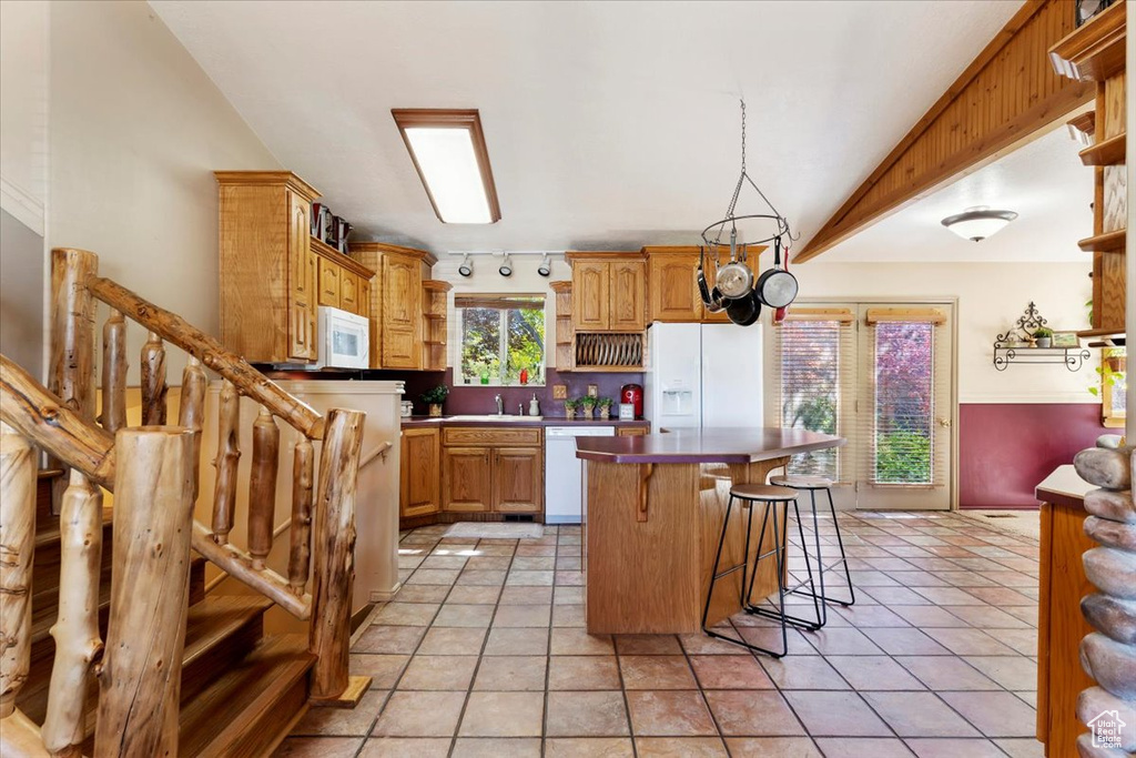 Kitchen featuring track lighting, white appliances, sink, light tile patterned floors, and a center island