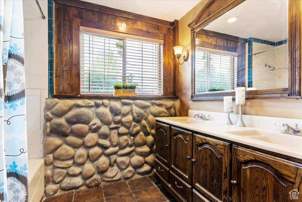 Bathroom featuring tile patterned floors, double sink vanity, wooden walls, and shower / bath combination with curtain