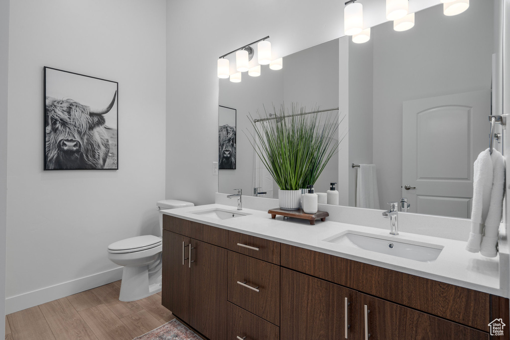 Bathroom with double vanity, wood-type flooring, and toilet