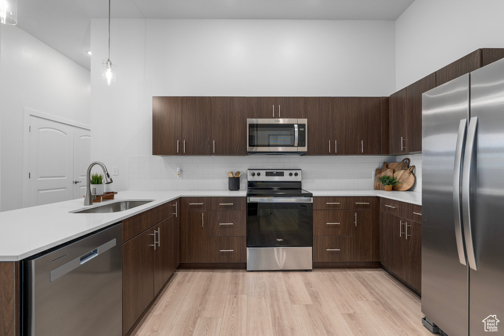 Kitchen with backsplash, stainless steel appliances, light hardwood / wood-style floors, a towering ceiling, and sink