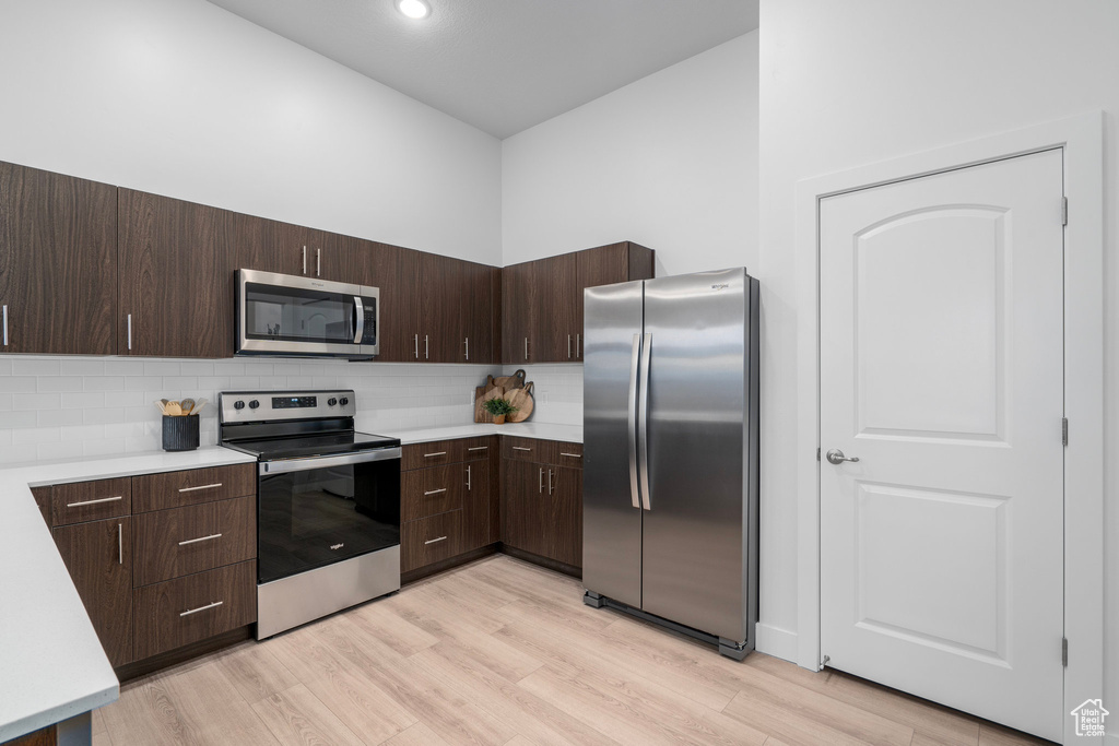 Kitchen featuring stainless steel appliances, dark brown cabinetry, tasteful backsplash, and light wood-type flooring