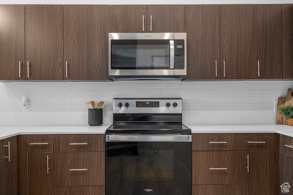 Kitchen with dark brown cabinetry, decorative backsplash, and appliances with stainless steel finishes