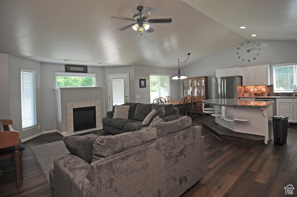 Living room with vaulted ceiling, a tiled fireplace, dark hardwood / wood-style floors, and plenty of natural light