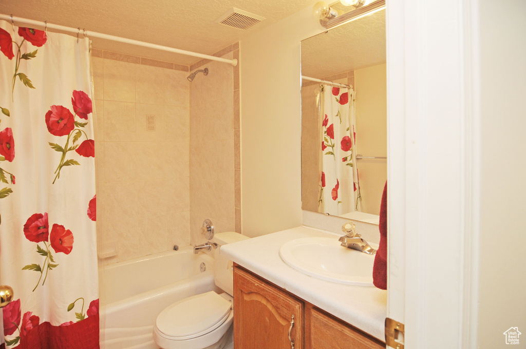 Full bathroom featuring vanity, shower / bathtub combination with curtain, a textured ceiling, and toilet