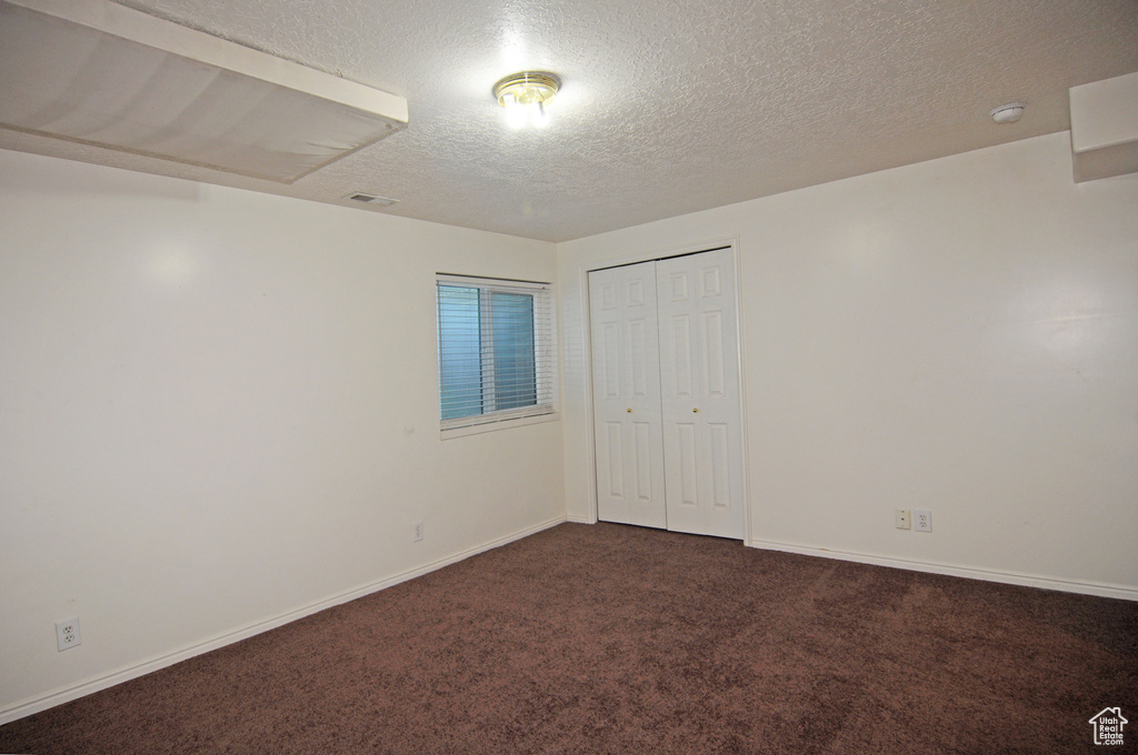 Unfurnished room featuring dark colored carpet and a textured ceiling