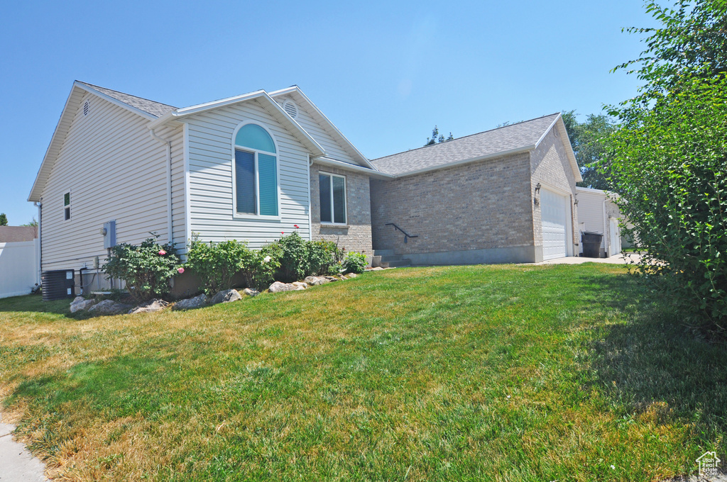 View of front of house with central air condition unit, a garage, and a front lawn