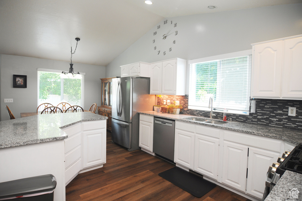 Kitchen featuring white cabinetry, stainless steel appliances, hanging light fixtures, decorative backsplash, and dark wood-type flooring