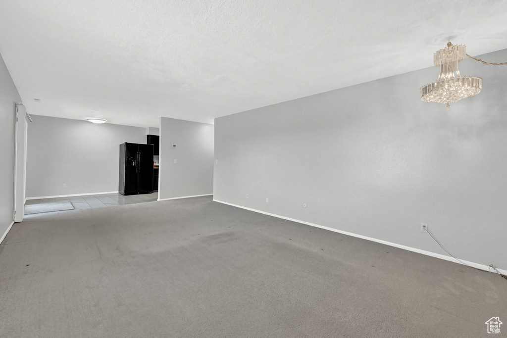 Unfurnished living room featuring a notable chandelier and carpet