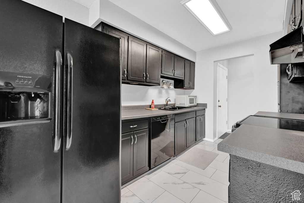 Kitchen with black appliances, sink, dark brown cabinetry, light tile patterned flooring, and wall chimney exhaust hood