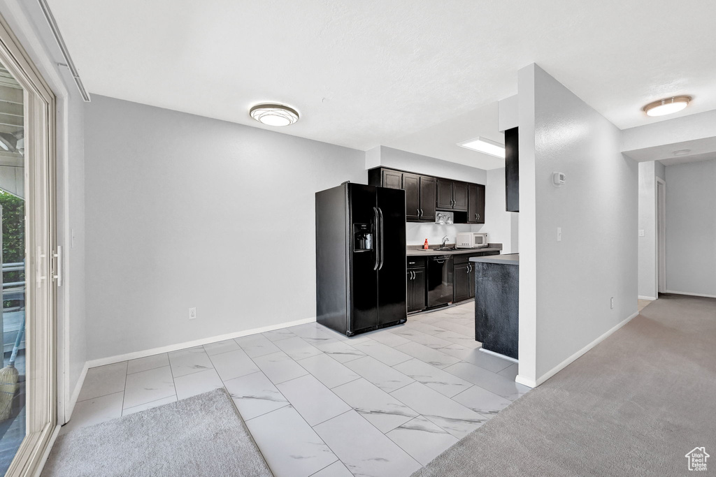 Kitchen featuring black appliances, light colored carpet, and dark brown cabinetry