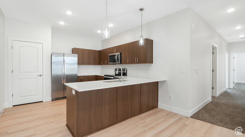 Kitchen featuring stainless steel appliances, pendant lighting, light colored carpet, kitchen peninsula, and backsplash