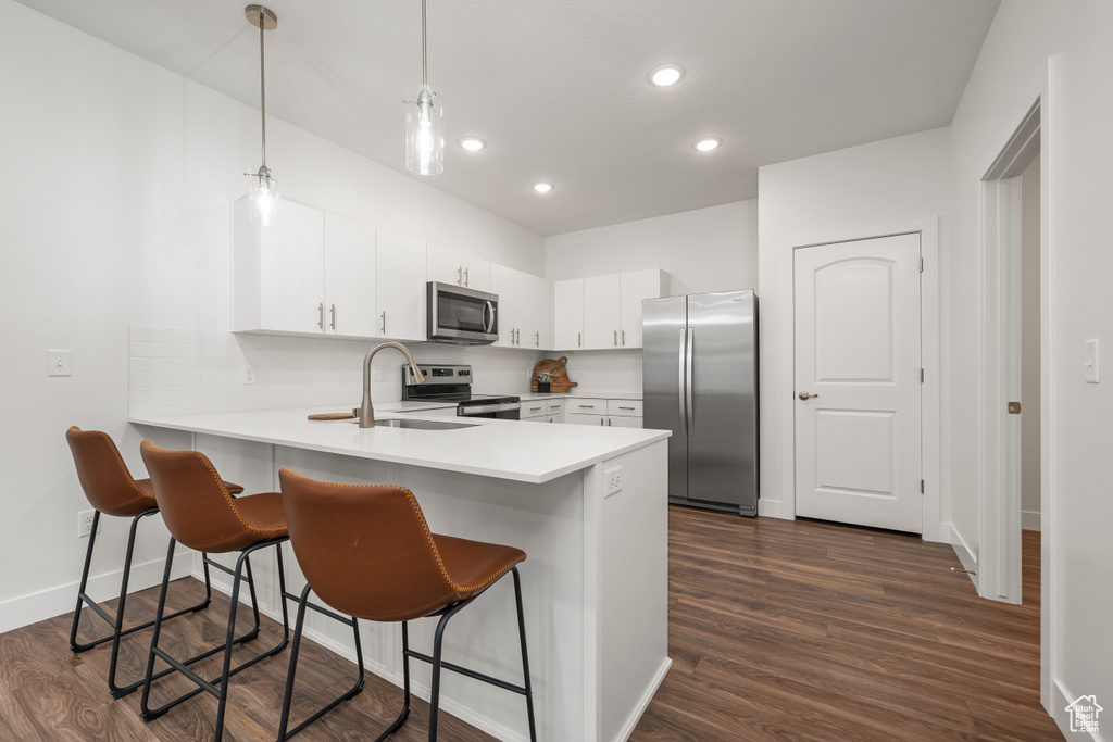 Kitchen with stainless steel appliances, pendant lighting, white cabinets, a breakfast bar area, and dark hardwood / wood-style floors