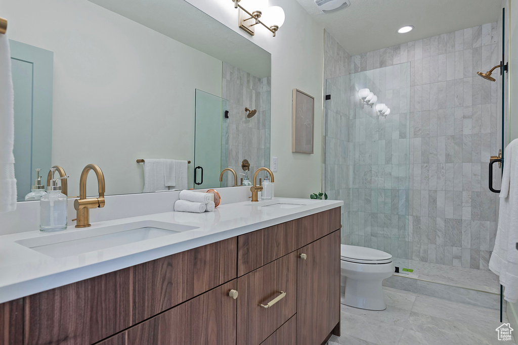 Bathroom featuring a shower with shower door, double vanity, toilet, and tile patterned floors