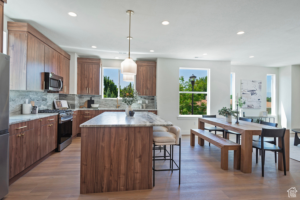 Kitchen with a center island, appliances with stainless steel finishes, light stone countertops, and hanging light fixtures