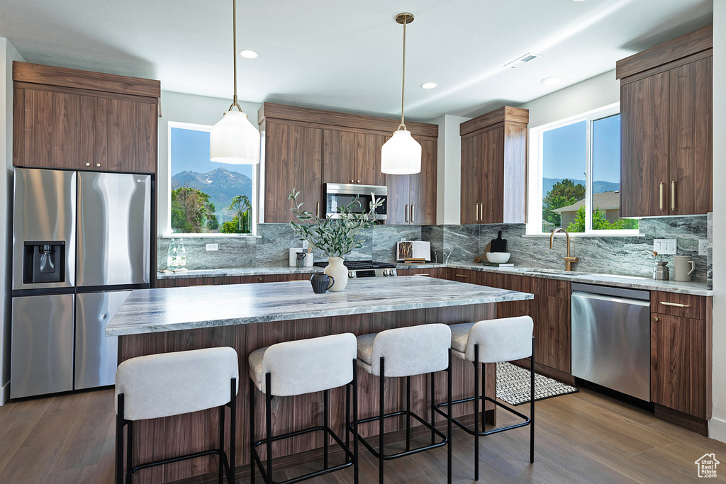 Kitchen featuring a kitchen island, appliances with stainless steel finishes, hanging light fixtures, and a healthy amount of sunlight