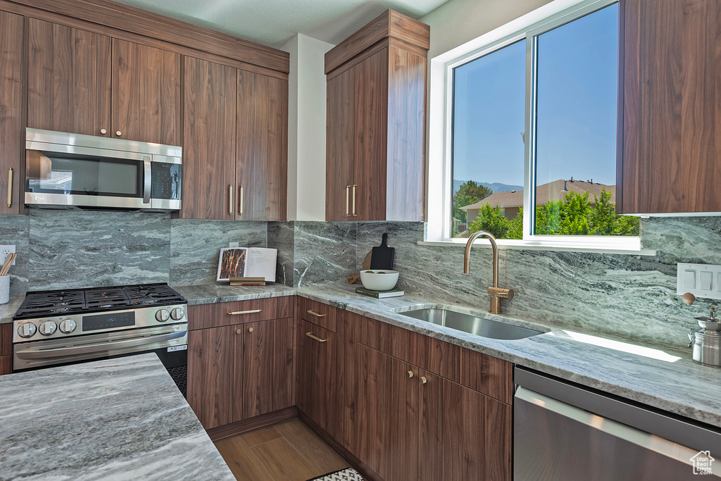 Kitchen featuring stainless steel appliances, light stone countertops, tasteful backsplash, and sink