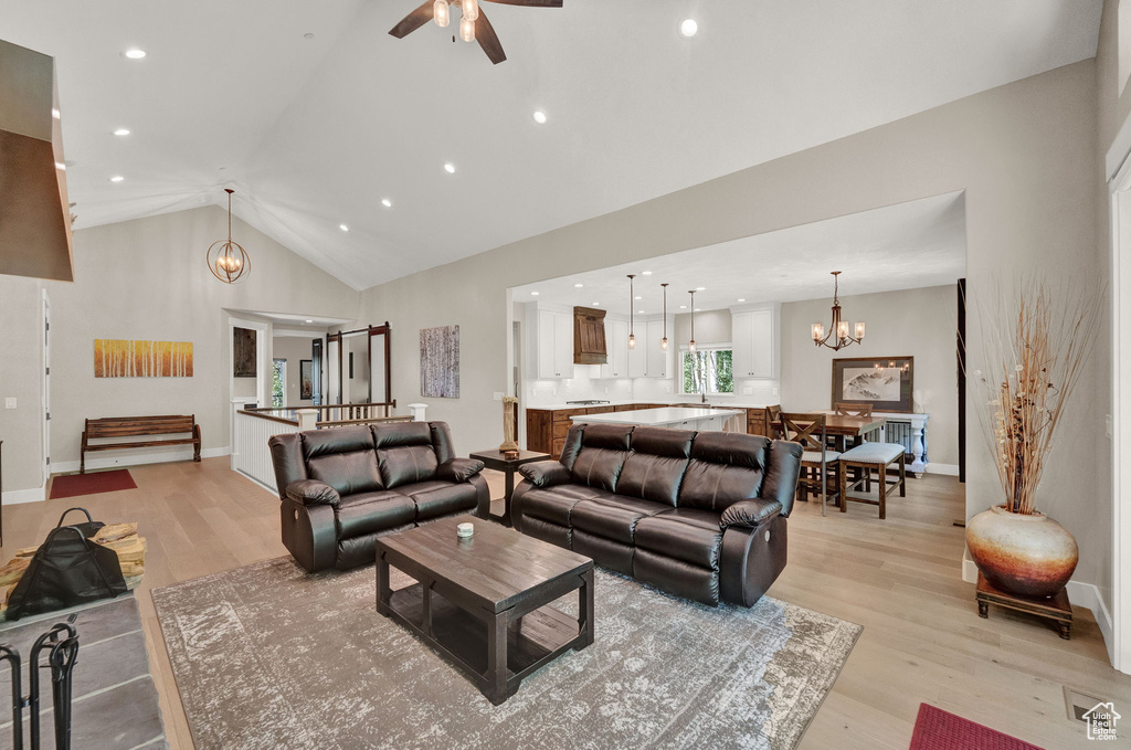 Living room featuring light hardwood / wood-style floors, ceiling fan with notable chandelier, and high vaulted ceiling