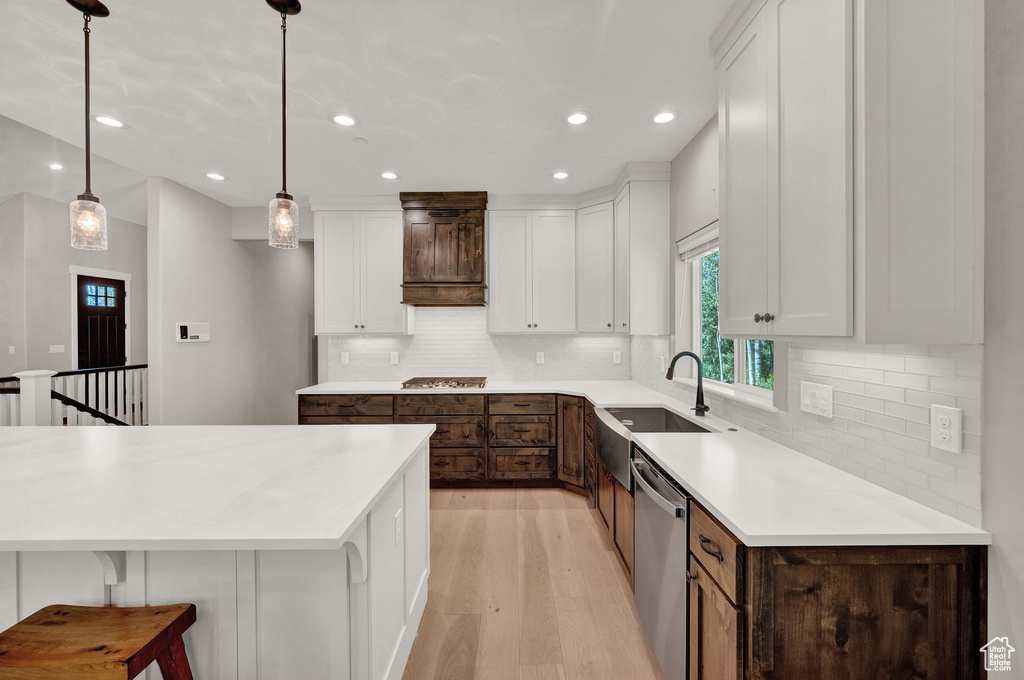 Kitchen featuring stainless steel appliances, light hardwood / wood-style floors, decorative light fixtures, decorative backsplash, and white cabinetry