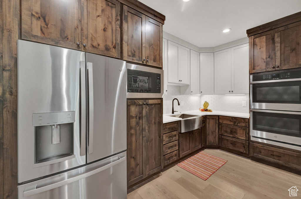 Kitchen with dark brown cabinets, light wood-type flooring, sink, appliances with stainless steel finishes, and backsplash