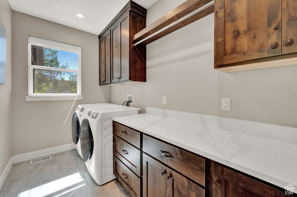 Clothes washing area featuring light tile patterned flooring, independent washer and dryer, and cabinets