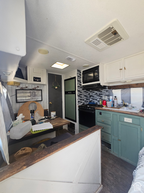 Kitchen featuring white cabinetry, range, blue cabinetry, black microwave, and backsplash