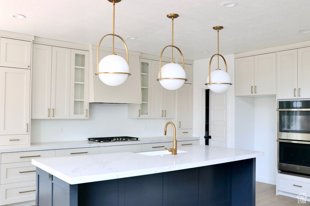 Kitchen featuring white cabinets, hardwood / wood-style flooring, stainless steel double oven, and a kitchen island with sink