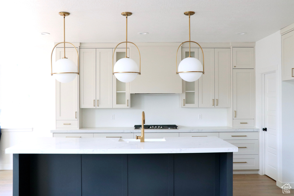 Kitchen with white cabinets, decorative light fixtures, light hardwood / wood-style flooring, and a center island with sink