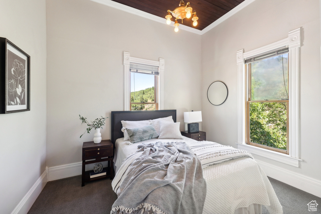 Bedroom with wood ceiling, crown molding, dark colored carpet, and an inviting chandelier