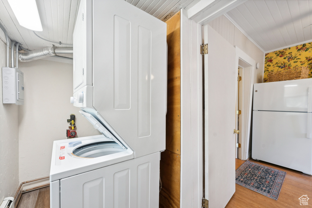 Laundry room featuring a baseboard radiator, crown molding, wood-type flooring, and stacked washer and dryer