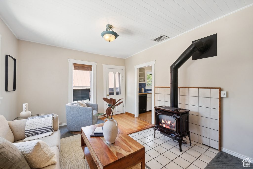 Living room featuring light hardwood / wood-style floors, a wood stove, a wealth of natural light, and crown molding