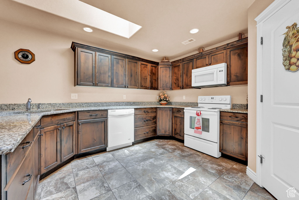 Kitchen featuring white appliances, sink, light stone counters, a skylight, and light tile patterned flooring