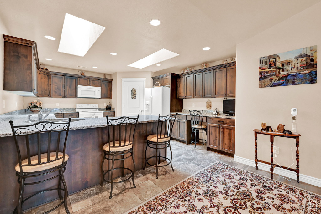 Kitchen with white appliances, a skylight, a breakfast bar area, light stone countertops, and light tile patterned floors