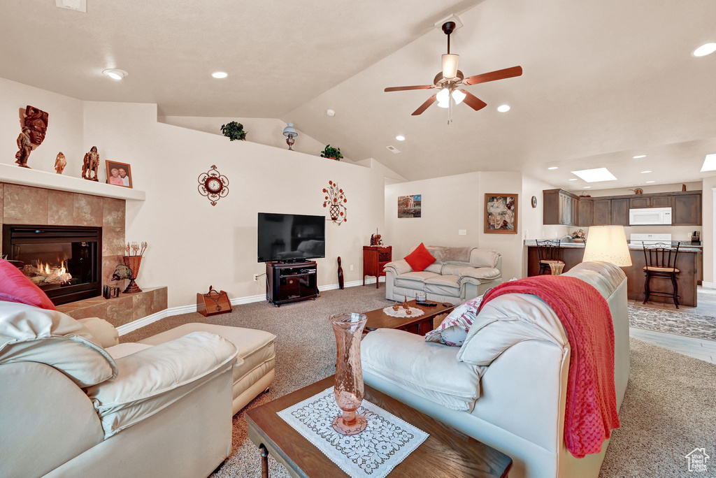 Carpeted living room with a fireplace, ceiling fan, and lofted ceiling