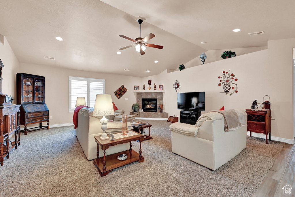 Carpeted living room with lofted ceiling, a tiled fireplace, and ceiling fan