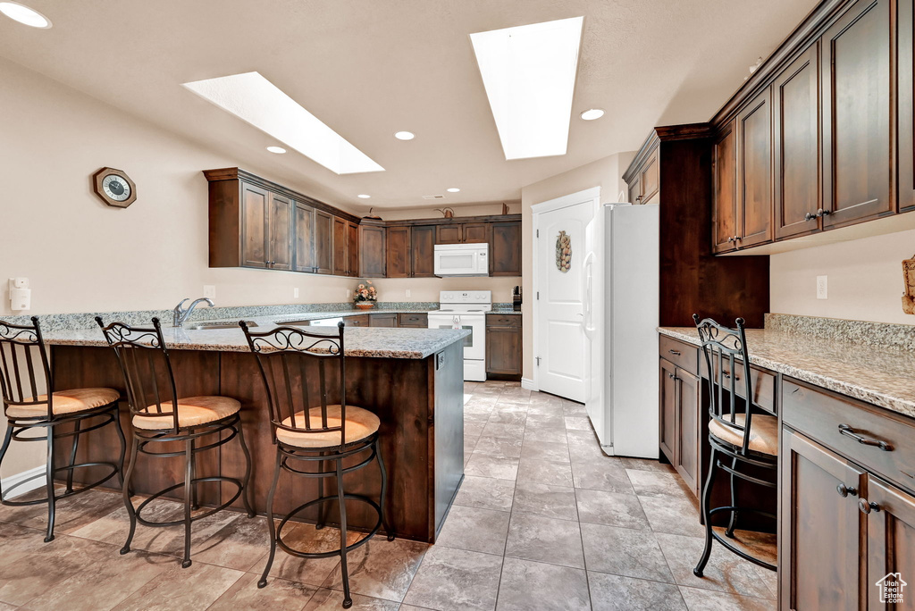 Kitchen with a breakfast bar, light tile patterned floors, light stone counters, and white appliances