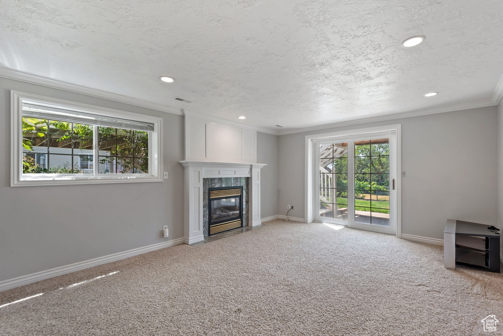 Unfurnished living room with a premium fireplace, carpet, a wealth of natural light, and crown molding