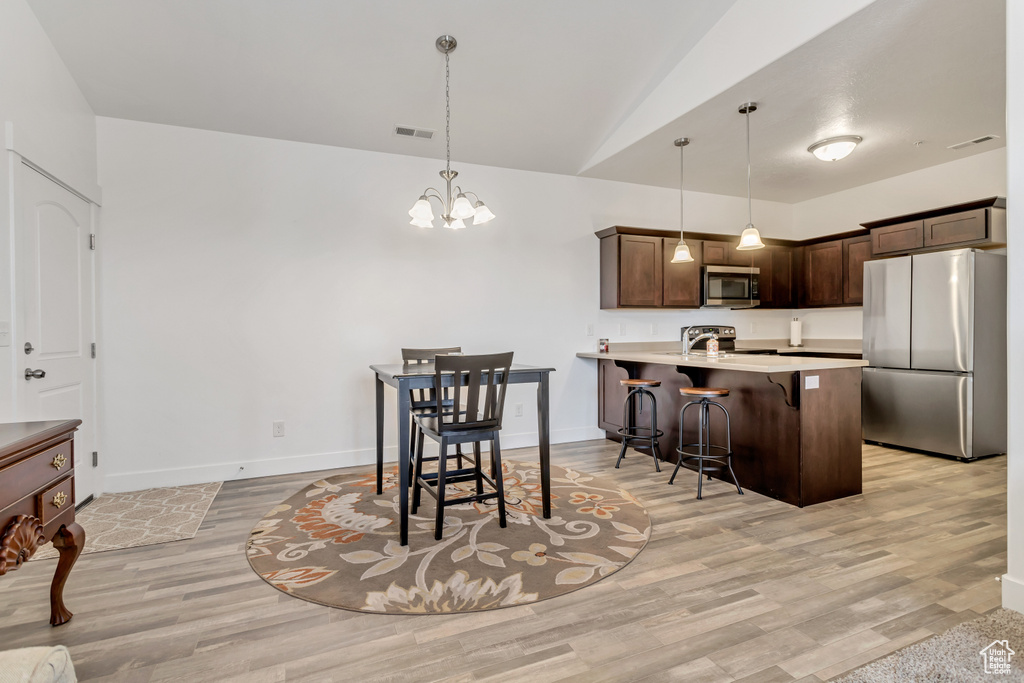 Kitchen featuring appliances with stainless steel finishes, light wood-type flooring, hanging light fixtures, and lofted ceiling