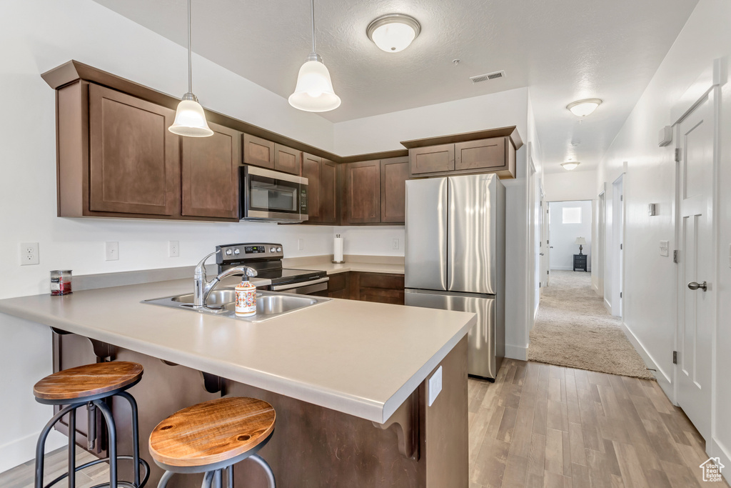 Kitchen with appliances with stainless steel finishes, a breakfast bar area, pendant lighting, kitchen peninsula, and light colored carpet