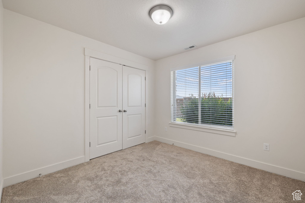 Unfurnished bedroom with light carpet and a closet