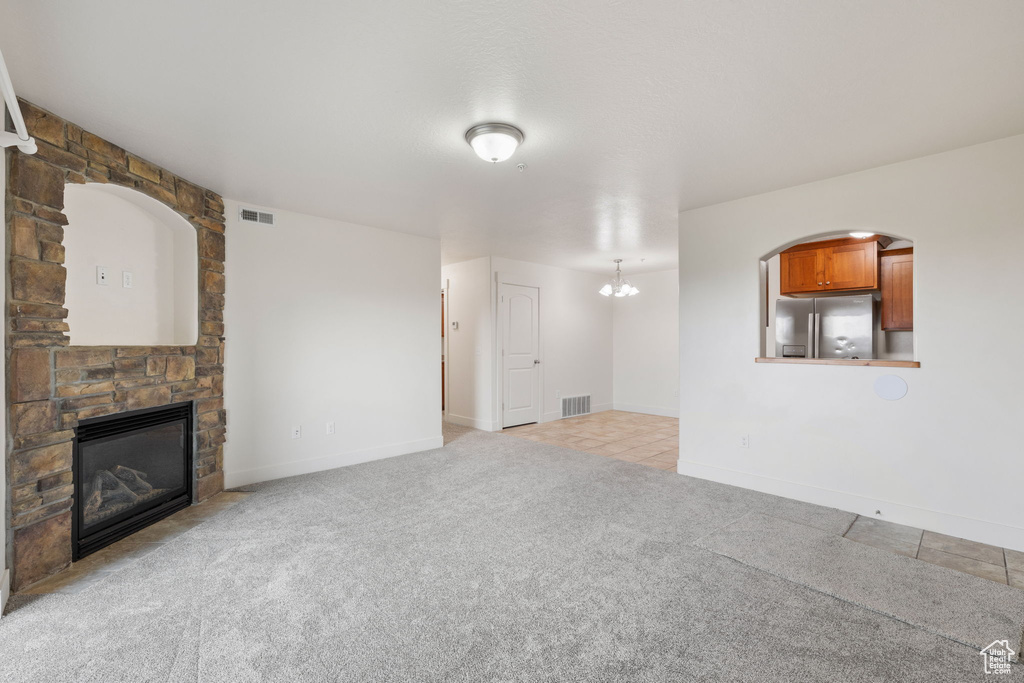 Unfurnished living room featuring a fireplace, a chandelier, and light colored carpet