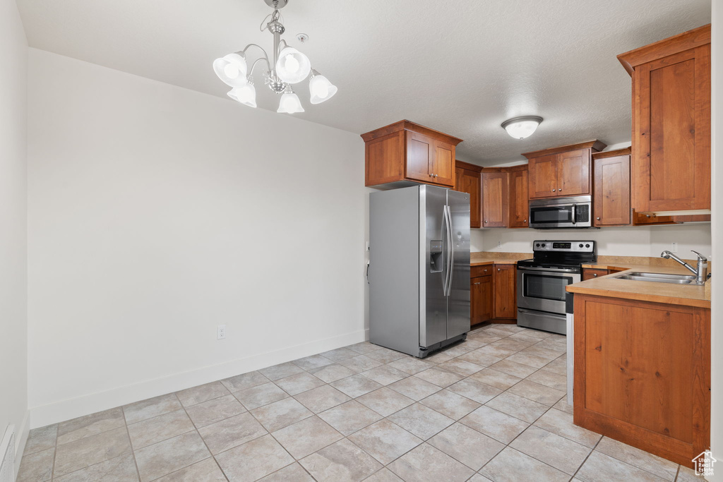 Kitchen with stainless steel appliances, sink, hanging light fixtures, light tile patterned flooring, and a notable chandelier