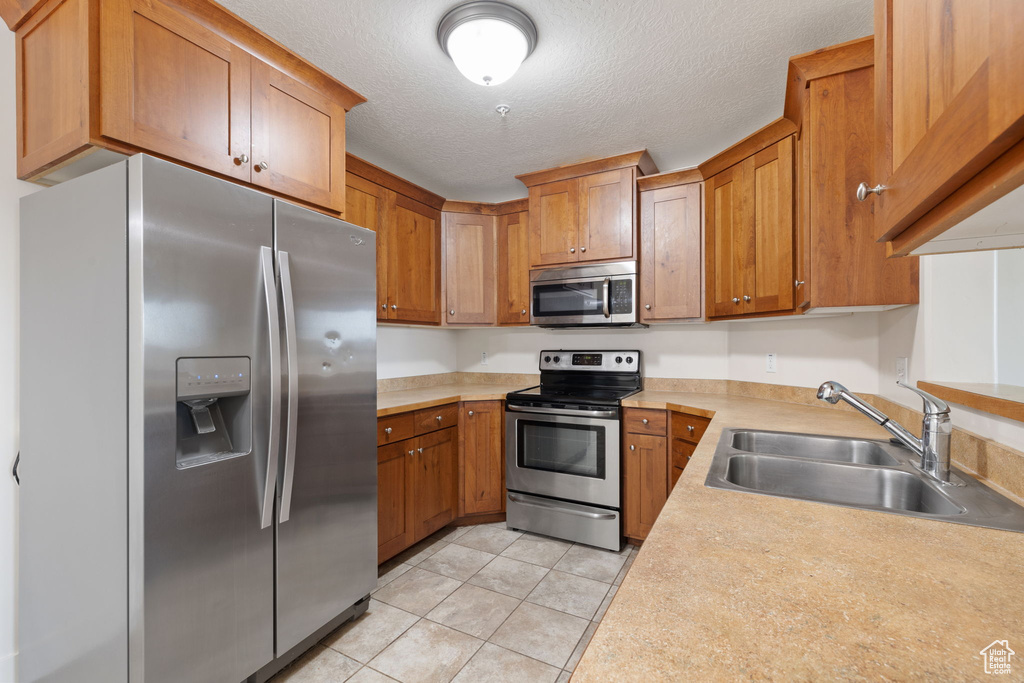 Kitchen with light tile patterned floors, stainless steel appliances, sink, and a textured ceiling