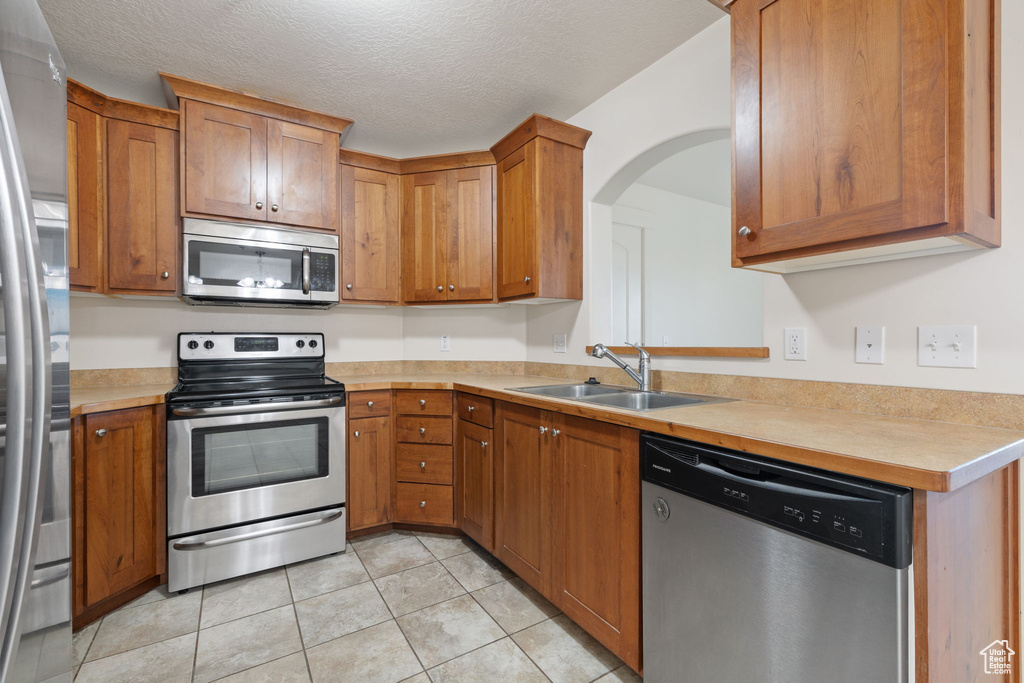 Kitchen with light tile patterned floors, stainless steel appliances, sink, and a textured ceiling