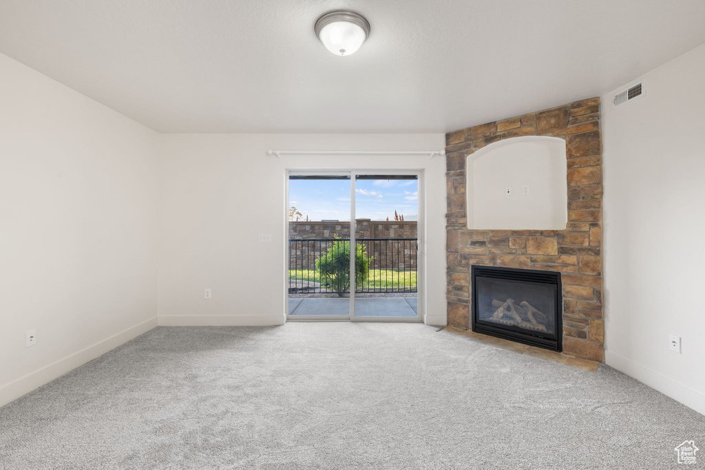 Unfurnished living room with a stone fireplace and carpet flooring